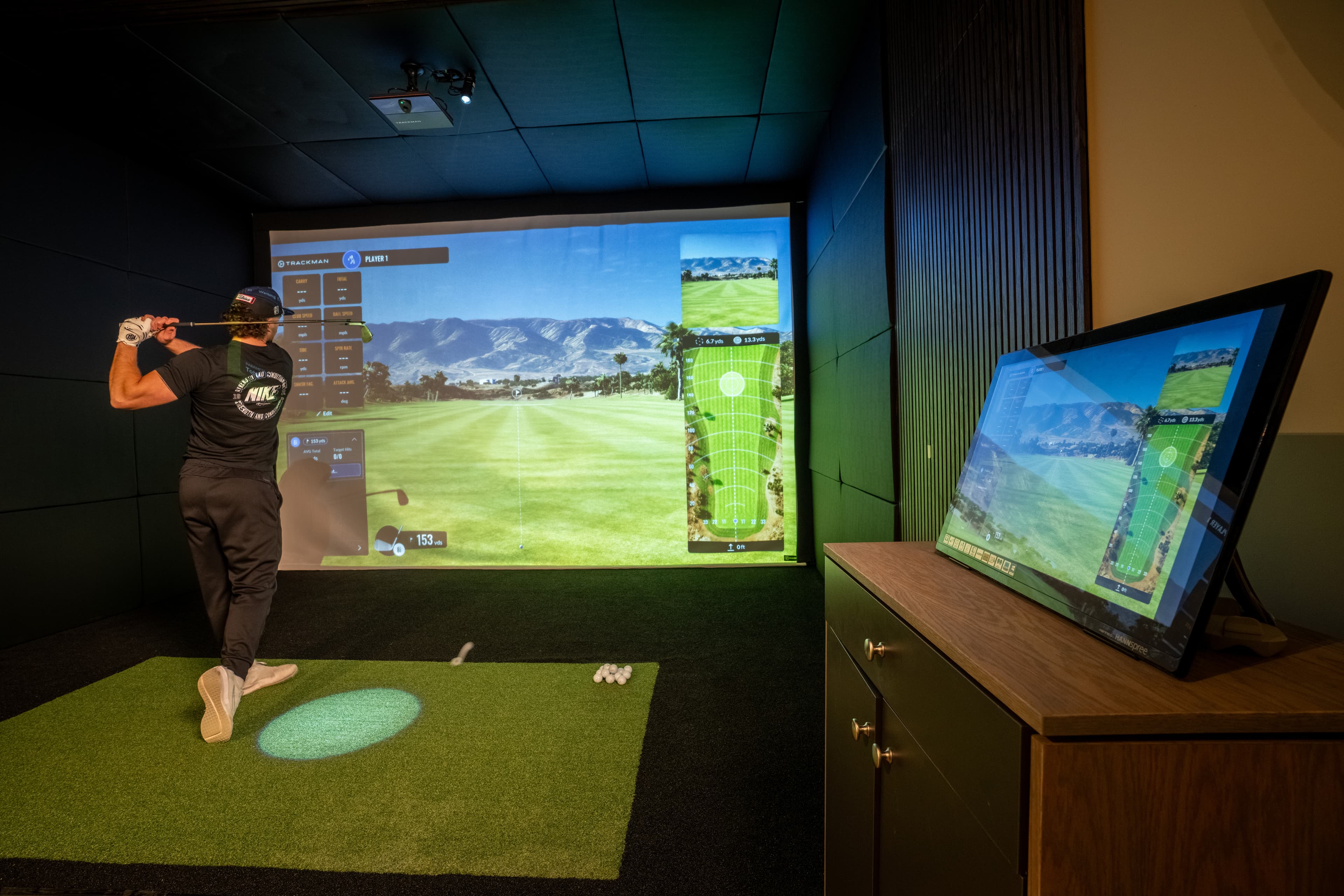 A golfer mid-swing in the Studio 22 simulator with TrackMan data on screen